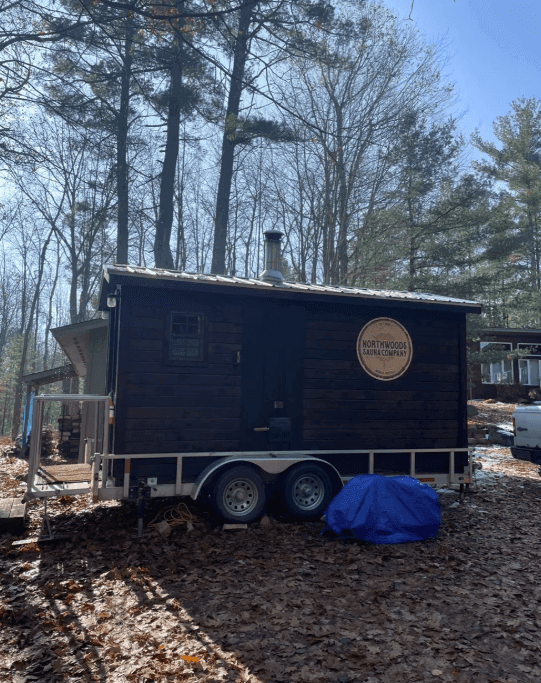 Dark sauna trailer overlooking a lake through bare trees
