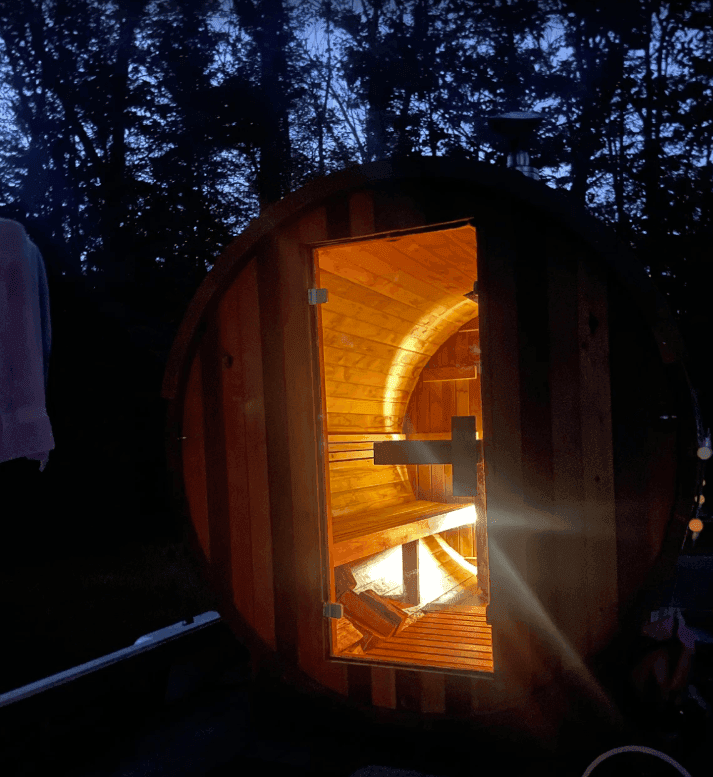 Open barrel sauna door revealing warmly lit wooden benches at dusk