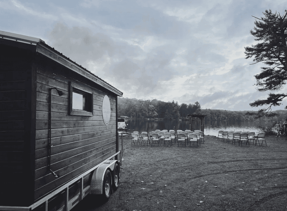 Dark sauna trailer beside a lake with rows of outdoor chairs