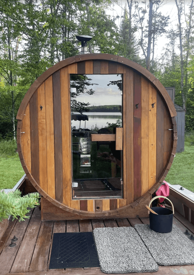 Glass entrance door of a barrel sauna on a wooden deck among trees