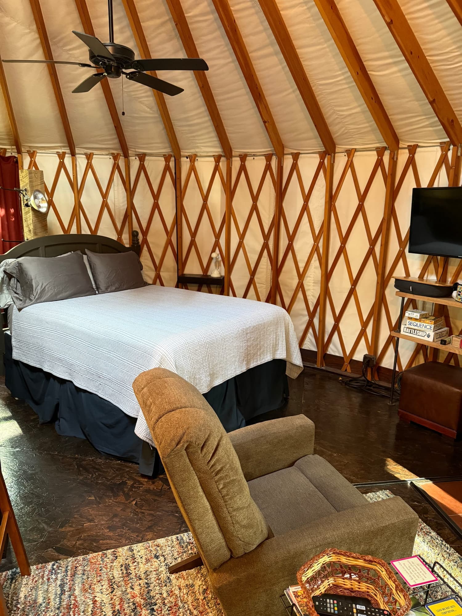 Bed and armchair beneath the yurt's wooden roof beams and ceiling fan