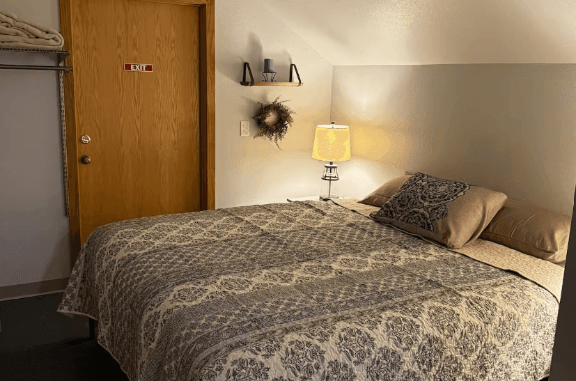 Bed with patterned bedding beside a wooden door and bedside lamp